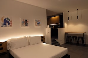 Una habitación de hotel moderna con una cama, obras de arte en la pared, un escritorio con taburetes y una zona de cocina.