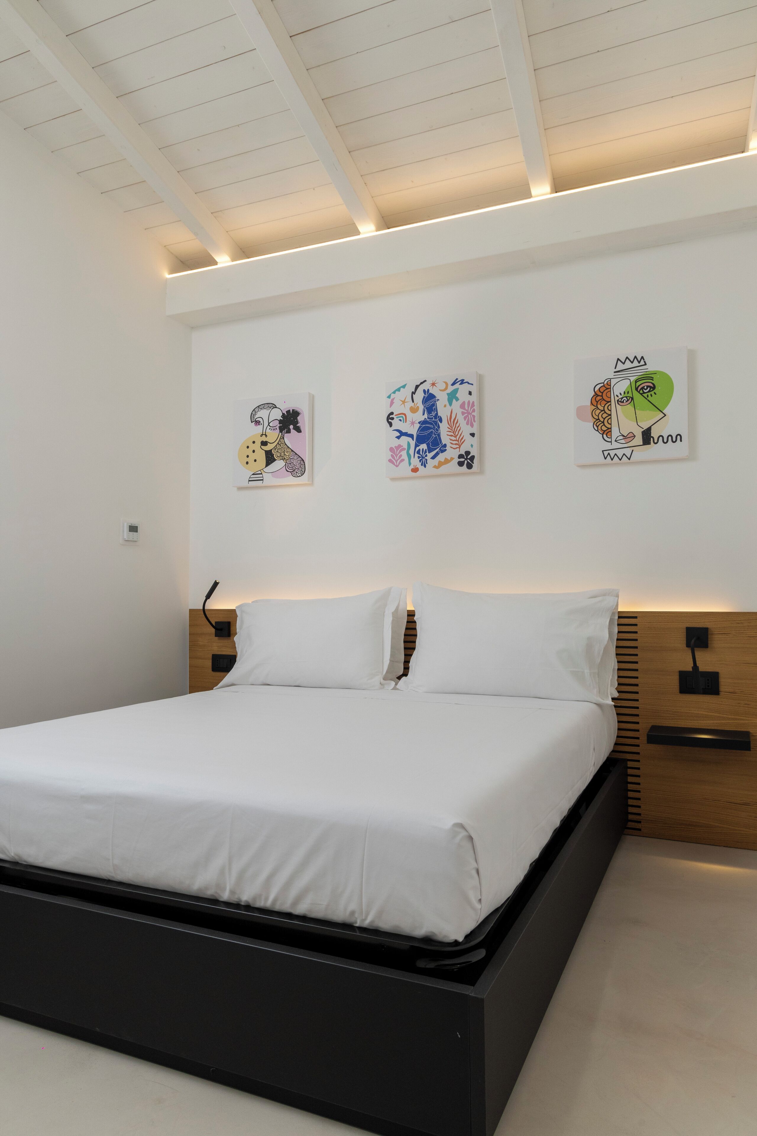 A modern bedroom with a bed, white walls, and artwork.