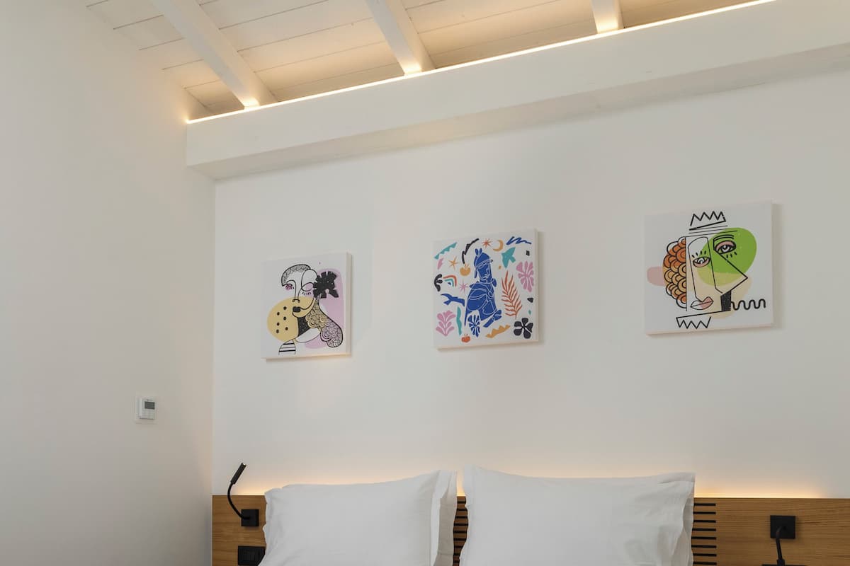 A modern bedroom with a bed, white walls, and artwork.