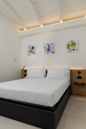 A modern bedroom with a bed, white walls, and artwork.