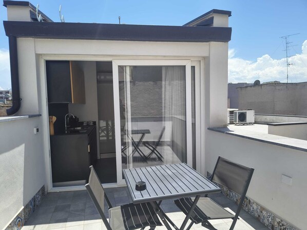A small balcony with a table and chairs, a sliding glass door, and an air conditioning unit.