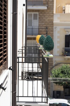 A balcony with metal railings, a white wall, and a window with blinds.