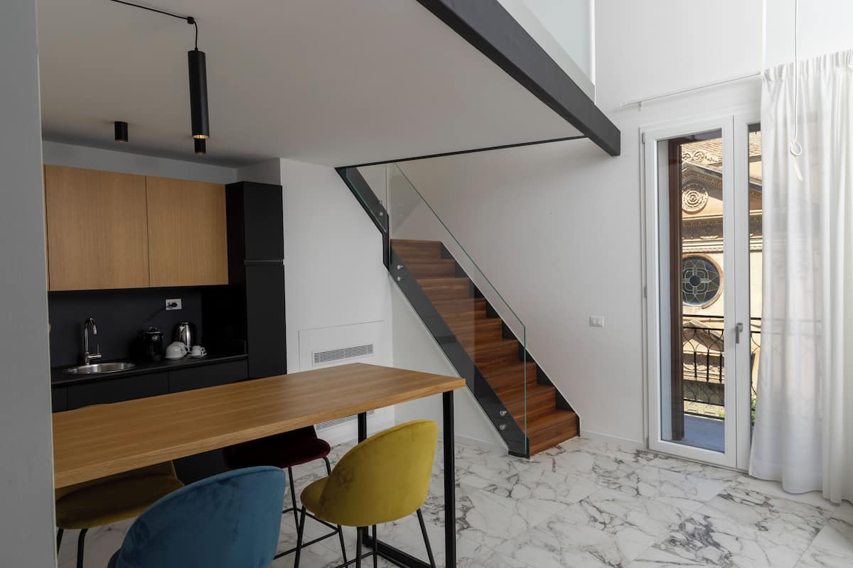A modern kitchen with a wooden table and chairs, a staircase, and a glass door leading to an outdoor area.