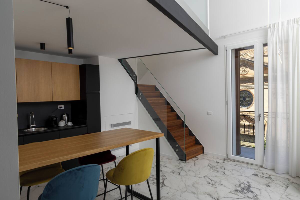 A modern kitchen with a wooden table and chairs, a staircase, and a glass door leading to an outdoor area.