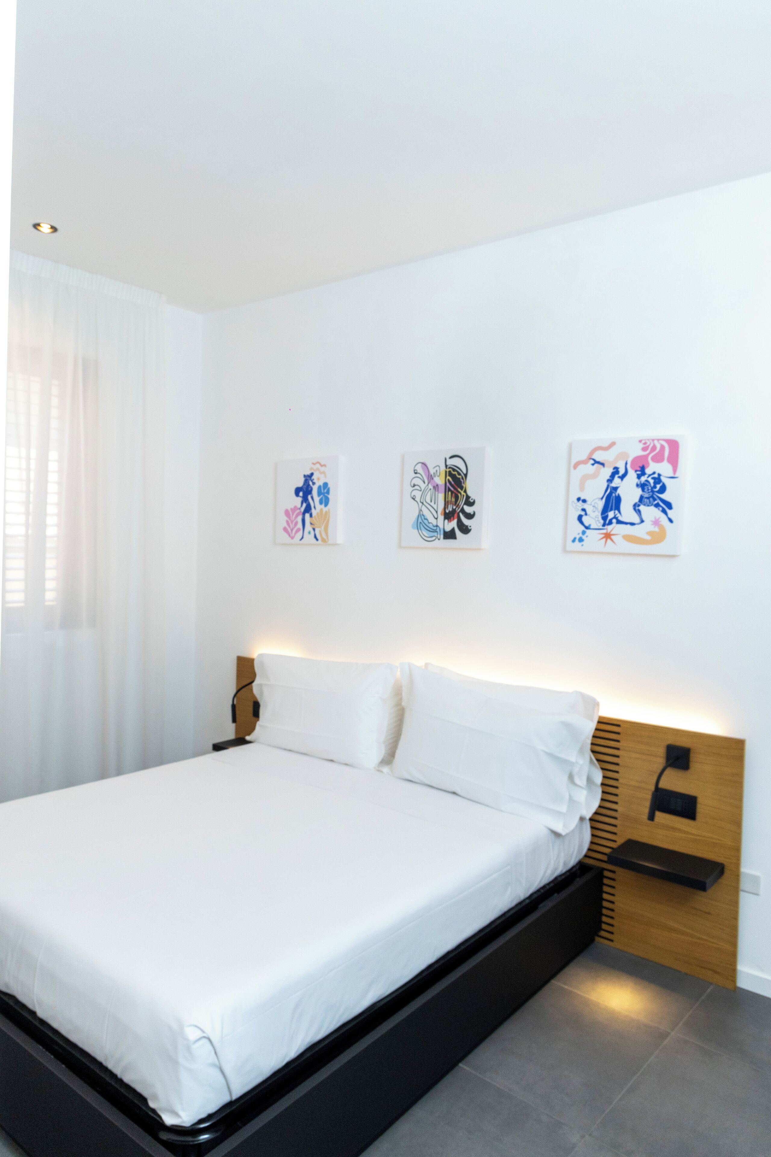 Ein modernes Schlafzimmer mit einem Bett, weißen Vorhängen und drei an der Wand befestigten Kunstwerken.