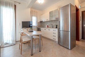 A modern kitchen with a stainless steel refrigerator, a dining table with chairs, and a TV. - Fibes Luxury Living 2 by Rentals Pro - Mouries Halkidiki (Mouries)