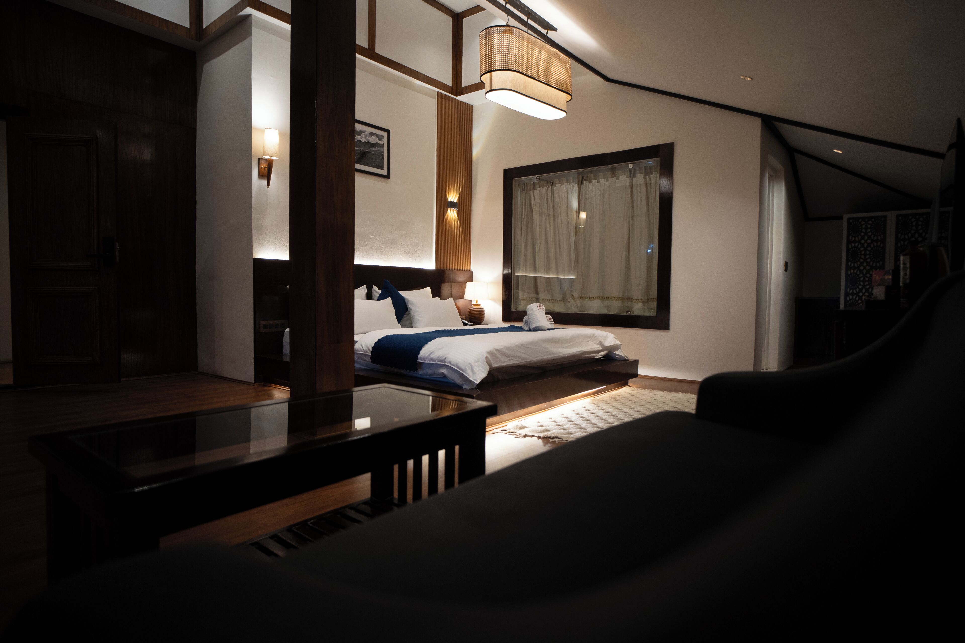 A hotel room with a bed, a nightstand, a lamp, a window with curtains, and a view of the outside.