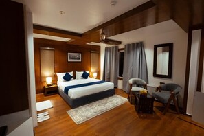 A bedroom with a large bed, bedside tables, a chair, a desk, and a window with curtains. - Walnut Village Resort (Pahalgam)