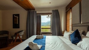 Quarto de hotel com uma cama grande, uma cadeira, uma escrivaninha e vista para montanhas pela janela.