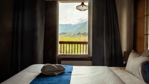 Quarto de hotel com cama, janela com vista para montanhas e luminária pendente.