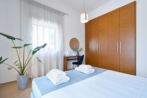 A bedroom with a bed, a wardrobe, a desk with a chair, a potted plant, and a hanging light fixture. - Villa Anastasia - Private Heated Pol (Chania)
