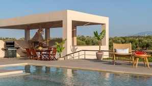A poolside area with a barbecue setup, outdoor seating, and a view of the landscape. - Villa Anastasia - Private Heated Pol (Chania)