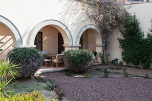 Ein Innenhof mit Bögen, einem Tisch, Stühlen und viel Grün.