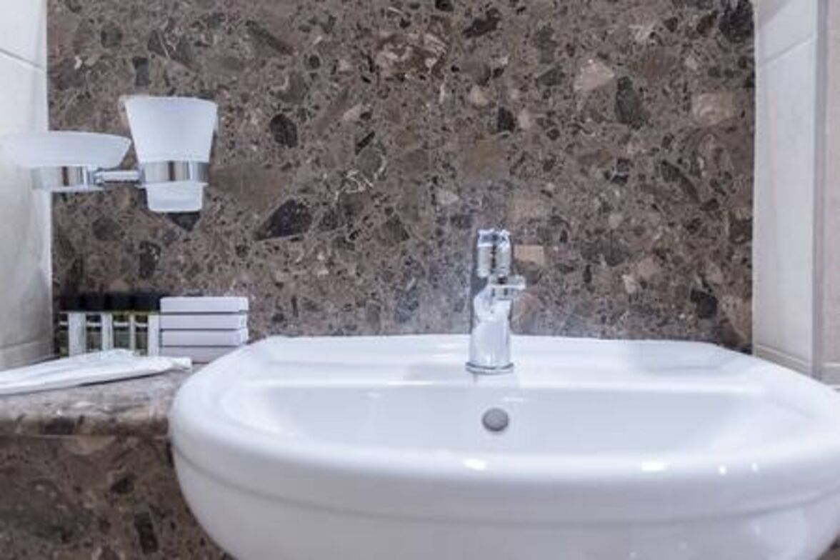 Un baño con lavamanos blanco, salpicadero de mármol e iluminación empotrada en la pared.