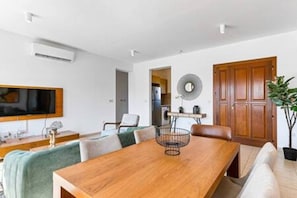 A modern dining area with a wooden table, chairs, a television, and a potted plant. - BF12 Adjacent to Aphrodite Hills - Pool & Terrace (Kouklia)
