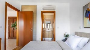 A bedroom with a bed, a wooden door, and a bathroom visible through an open door. - BF12 Adjacent to Aphrodite Hills - Pool & Terrace (Kouklia)
