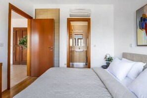 A bedroom with a bed, a wooden door, and a bathroom visible through an open door. - BF12 Adjacent to Aphrodite Hills - Pool & Terrace (Kouklia)