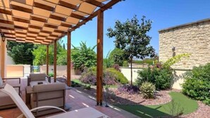Een overdekt terras met tuinmeubilair, een stenen muur en een aangelegde tuin.