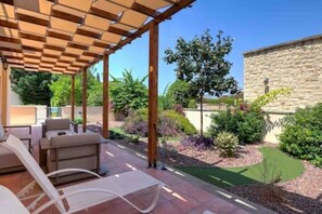 A covered patio with outdoor furniture, a stone wall, and landscaped garden. - L02 Adjacent to Aphrodite Hills - Pool & Patio (Kouklia)