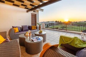 A balcony with wicker furniture, a small table, and a view of a green landscape. - HG07 Adjacent to Aphrodite Hill - Pool & Terrace (Kouklia)