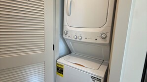 Un lavadero pequeño con lavadora y secadora de carga frontal, una puerta con listones horizontales y suelo de madera.