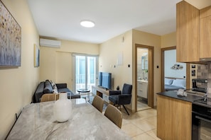 A modern kitchen with a dining area, a TV, and a view to the outside.