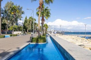 Une piscine avec une allée dallée, des palmiers et une vue sur la mer.
