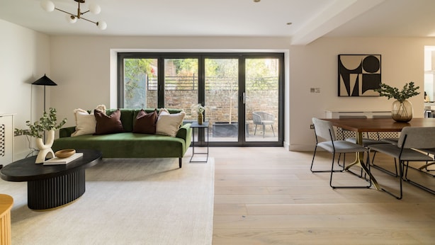 A modern living room with a green sofa, a dining table with chairs, a black coffee table, and a large sliding glass door leading to an outdoor area. - Sage Tones with Private Patio (London)