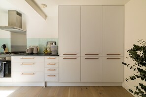 A modern kitchen with white cabinets, wooden handles, and a stainless steel range hood. - Sage Tones with Private Patio (London)