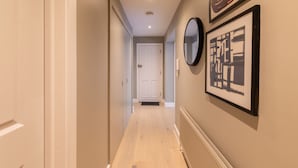 A hallway with a white door at the end, a radiator on the right, and framed artwork on the wall. - Sage Tones with Private Patio (London)