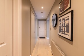 A hallway with a white door at the end, a radiator on the right, and framed artwork on the wall. - Sage Tones with Private Patio (London)