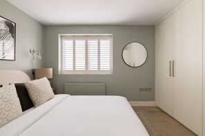 A bedroom with a bed, a round mirror, a window with blinds, a radiator, and a wardrobe. - Sage Tones with Private Patio (London)