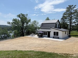 Une maison à deux étages dotée d’une grande terrasse, d’un patio couvert et offrant une vue sur un lac.