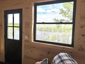 A cabin interior with a large window overlooking a lake and trees.