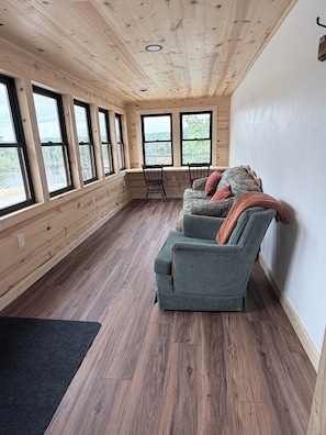 A spacious room with wooden walls and floors, large windows, a green sofa, and a wooden ceiling.