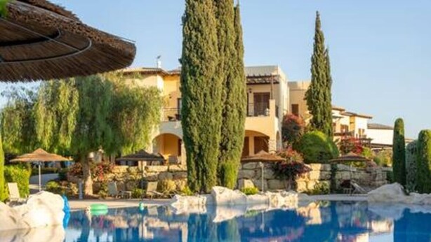 Una piscina con borde de piedra, rodeada de árboles y un edificio con arcos.