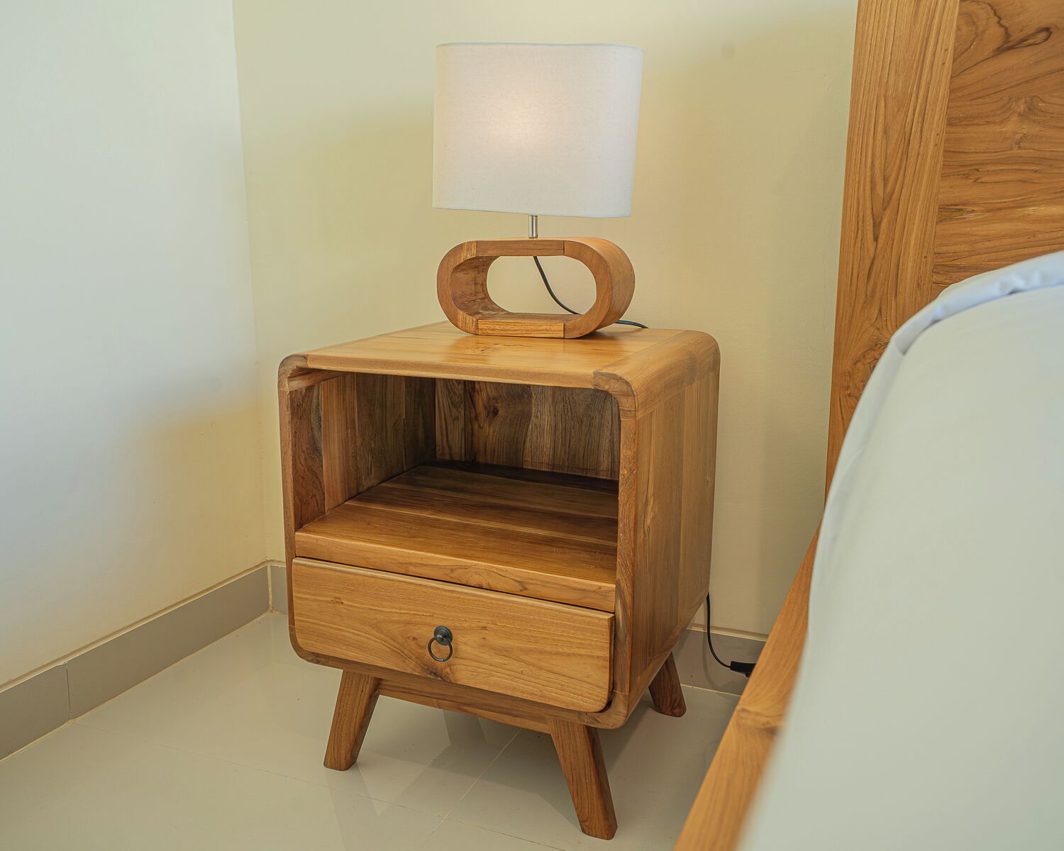 A wooden bedside table with a lamp, a drawer, and a power outlet.