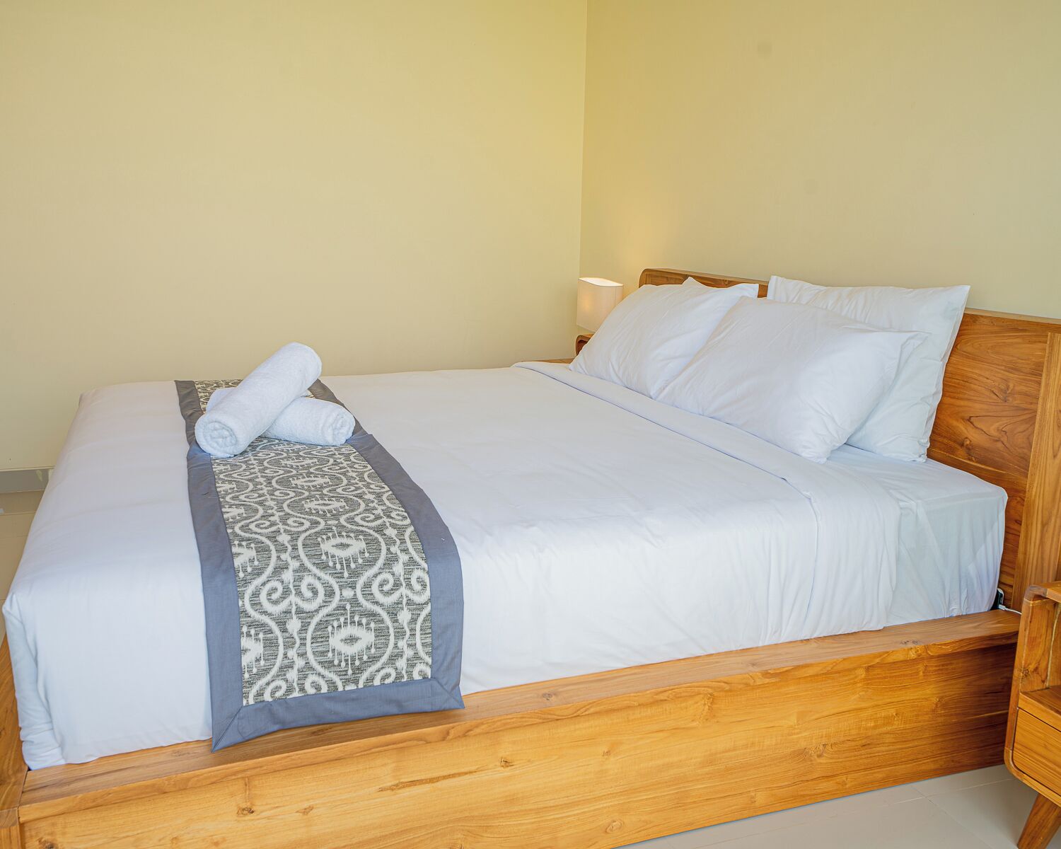 A neatly made bed with white linens, a patterned throw, and a wooden headboard.