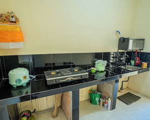 A kitchen with a gas stove, a rice cooker, a sink, and a small window.