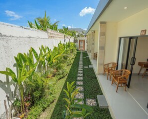 A hotel corridor with a tiled pathway, indoor seating area, and a white wall with plants.
