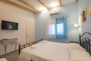 Ein Schlafzimmer mit Bett, Fernseher, Klimaanlage, einem Fenster mit Vorhängen und einer Nachttischlampe.