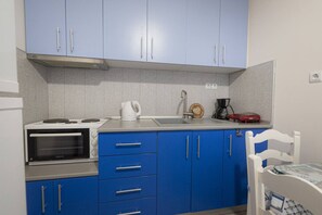 Une cuisine compacte équipée d’un four encastré, d’une machine à café et d’une bouilloire posées sur le plan de travail.