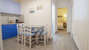 Kompakti keittiö, jossa on siniset kaapit, ruokapöytä tuoleineen sekä käytävä, joka johtaa makuuhuoneeseen.