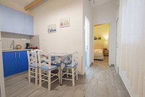 Une cuisine de taille réduite avec des meubles bleus, une table à manger avec des chaises et un couloir menant à une chambre.