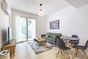 A modern living room with a sofa, coffee table, and chairs, a TV, and a staircase leading to an outdoor area.