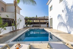 A swimming pool with a pergola, lounge chairs, and a palm tree.