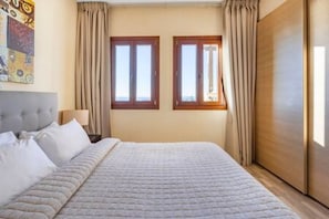 Ein Schlafzimmer mit einem großen Bett, zwei Fenstern, einem Kleiderschrank und einem Nachttisch.