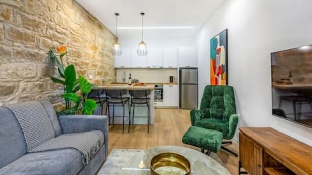 A modern living room with a sofa, a green armchair, a coffee table, and a TV. - Olga Apt 1 - 1bdr apartment on ground floor (Limassol)
