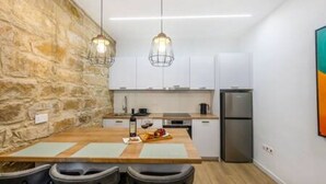 A modern kitchen with a stone accent wall, pendant lights, and a dining area with chairs and a table. - Olga Apt 1 - 1bdr apartment on ground floor (Limassol)