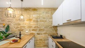 A kitchen with a stone wall, wooden countertop, white cabinets, and pendant lighting. - Olga Apt 1 - 1bdr apartment on ground floor (Limassol)